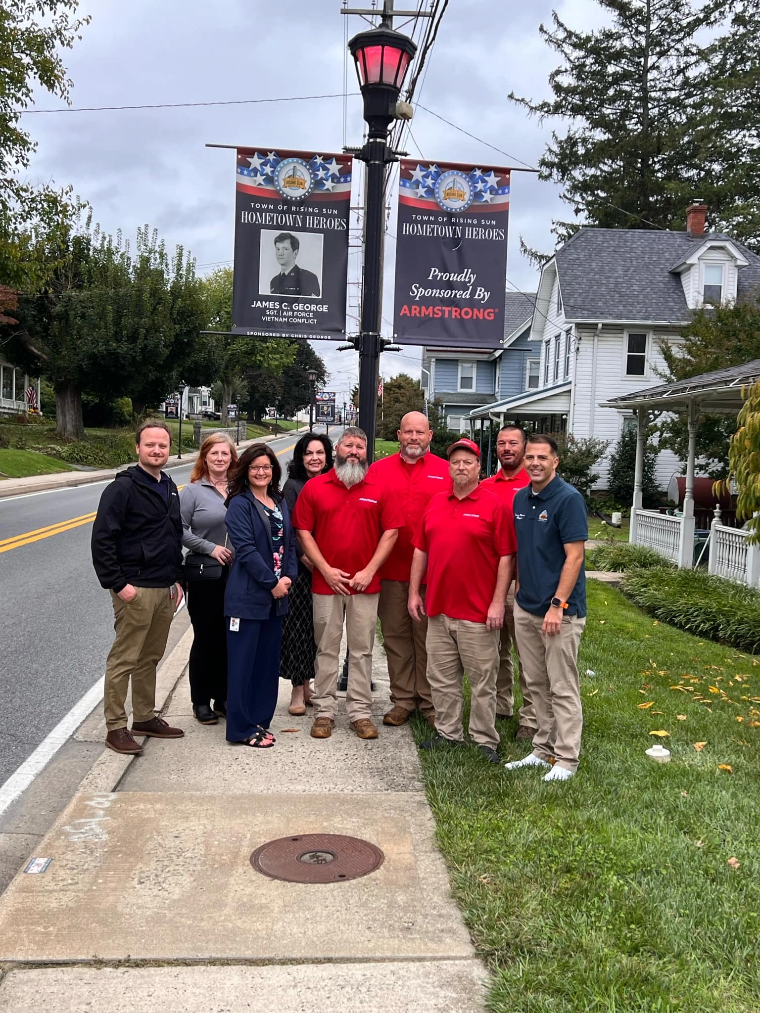 Rising Sun team posing in front of lamp post with Veterans Banner